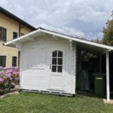Una graziosa casetta in legno bianco con un piccolo portico, circondata da alberi fioriti